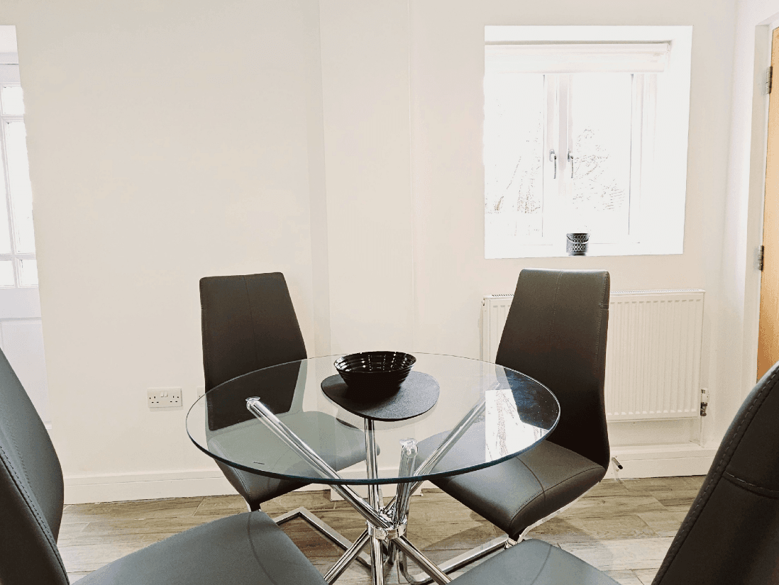 Contemporary dining area with round glass table and four black chairs at The Maple Suite, Oakdale Apartments Contemporary dining area with round glass table and four black chairs at The Maple Suite, Oakdale Apartments