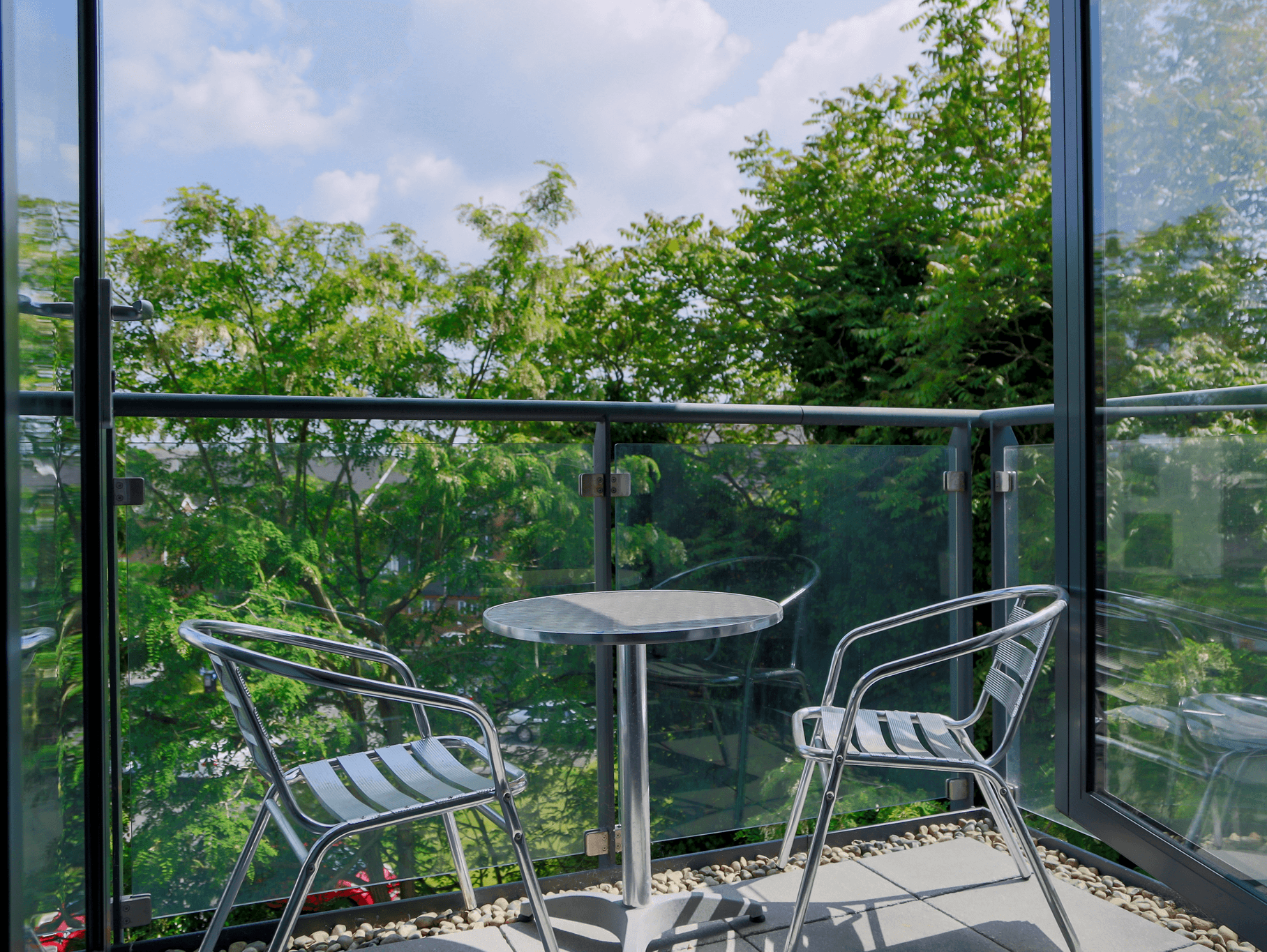 Glass-panel balcony with bistro table and chairs overlooking greenery at The Willow Suite, Cardinal Place, Woking Glass-panel balcony with bistro table and chairs overlooking greenery at The Willow Suite, Cardinal Place, Woking
