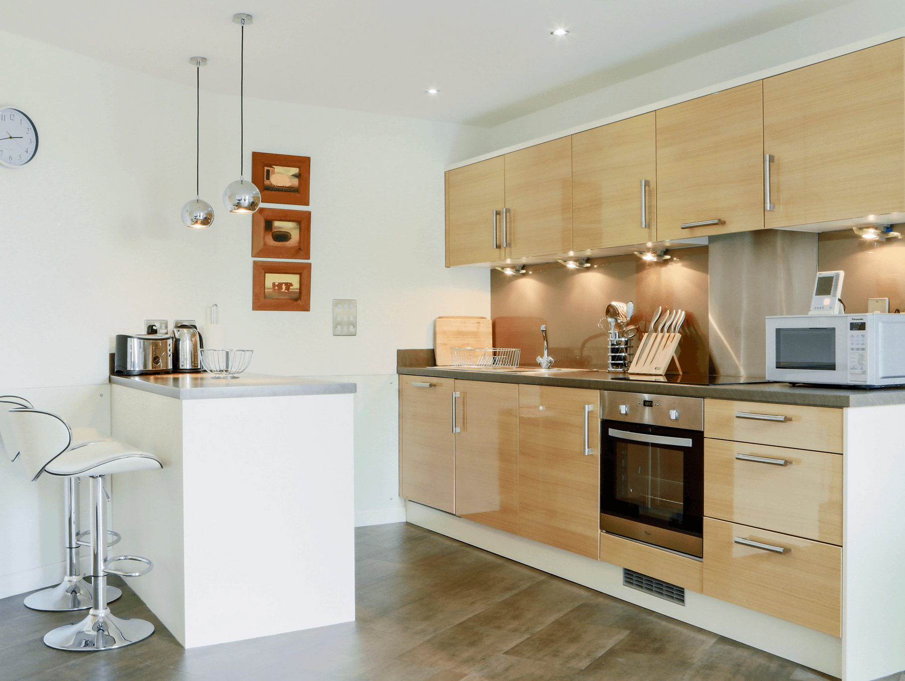 Contemporary open-plan kitchen with wood cabinetry, integrated appliances, and breakfast bar at The Willow Suite, Cardinal Place, Woking Contemporary open-plan kitchen with wood cabinetry, integrated appliances, and breakfast bar at The Willow Suite, Cardinal Place, Woking