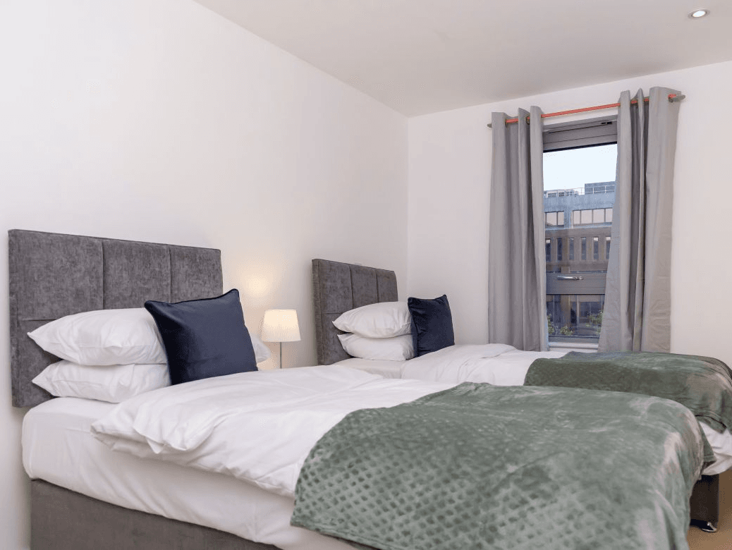 Twin bedroom with grey headboards, green throw blankets, and window at The Sycamore Suite, Enterprise Place, Woking Twin bedroom with grey headboards, green throw blankets, and window at The Sycamore Suite, Enterprise Place, Woking