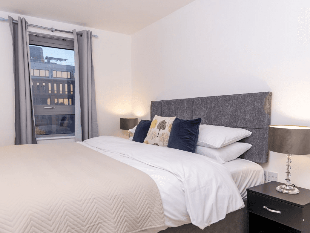 King bedroom with plush duvet, bedside lamps, and balcony view at The Sycamore Suite, Enterprise Place, Woking King bedroom with plush duvet, bedside lamps, and balcony view at The Sycamore Suite, Enterprise Place, Woking