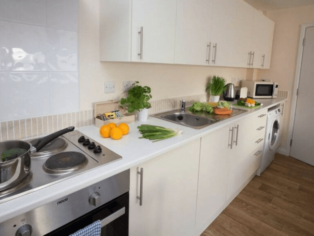 Long white kitchen with modern cabinetry, oven, fresh herbs, and orange fruit in serviced apartment – Castle 6 - Southampton Long white kitchen with modern cabinetry, oven, fresh herbs, and orange fruit in serviced apartment – Castle 6 - Southampton