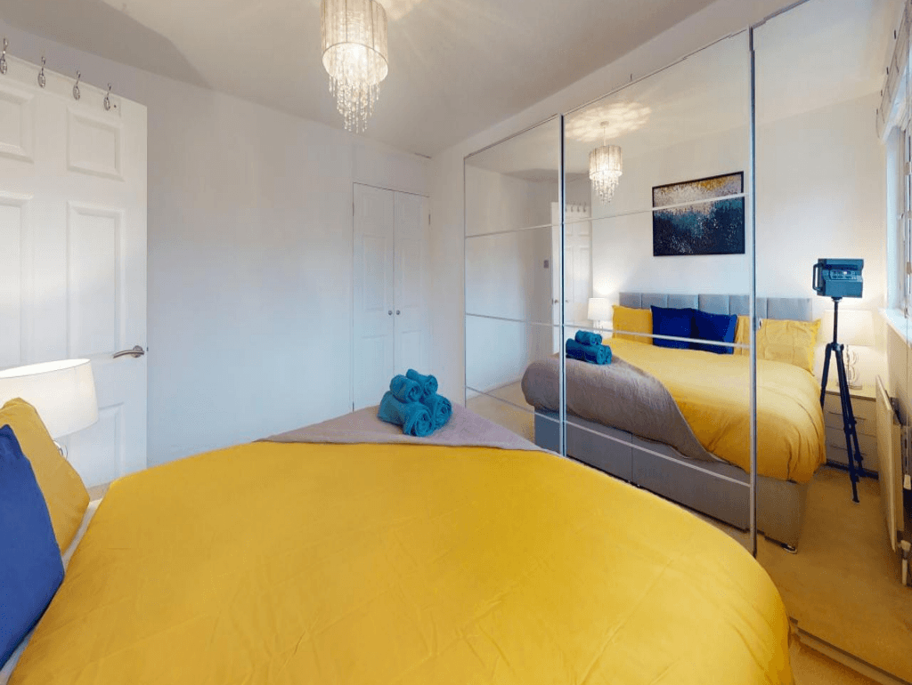 Double bedroom with mustard yellow throw, two blue accent pillows, mirrored wardrobe and large window – Parlaunt House - Slough Double bedroom with mustard yellow throw, two blue accent pillows, mirrored wardrobe and large window – Parlaunt House - Slough