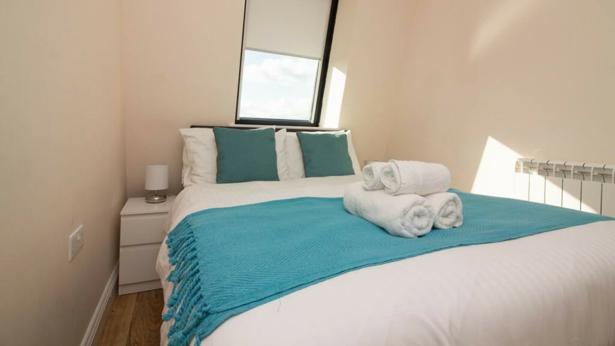 Bright bedroom with king-size bed, blue throw and two white towels, bedside tables, and window – Castle 17 - Southampton Bright bedroom with king-size bed, blue throw and two white towels, bedside tables, and window – Castle 17 - Southampton