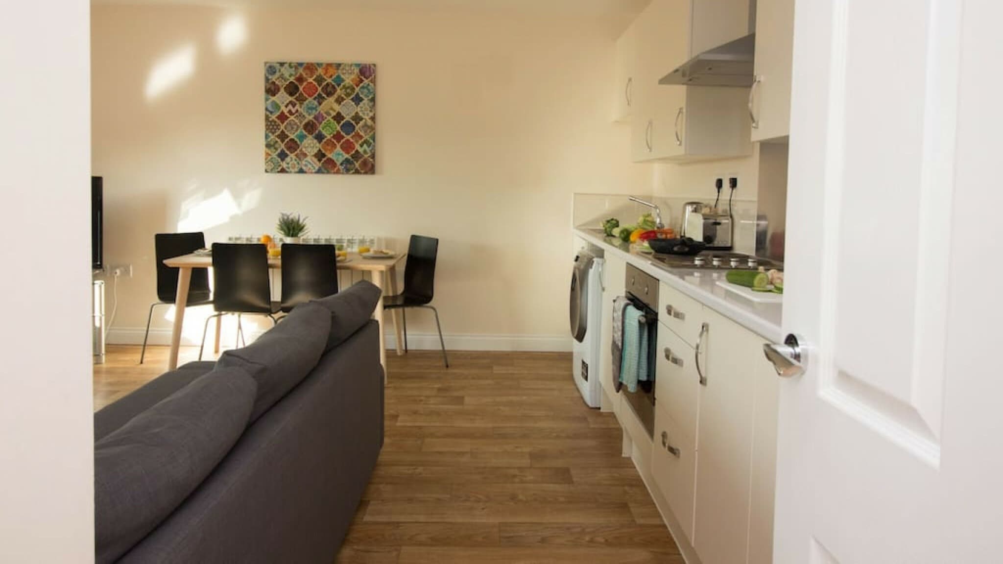 Dining table and chairs with kitchen appliances, wall-mounted art, and modern lighting – Castle 17 - Southampton Dining table and chairs with kitchen appliances, wall-mounted art, and modern lighting – Castle 17 - Southampton