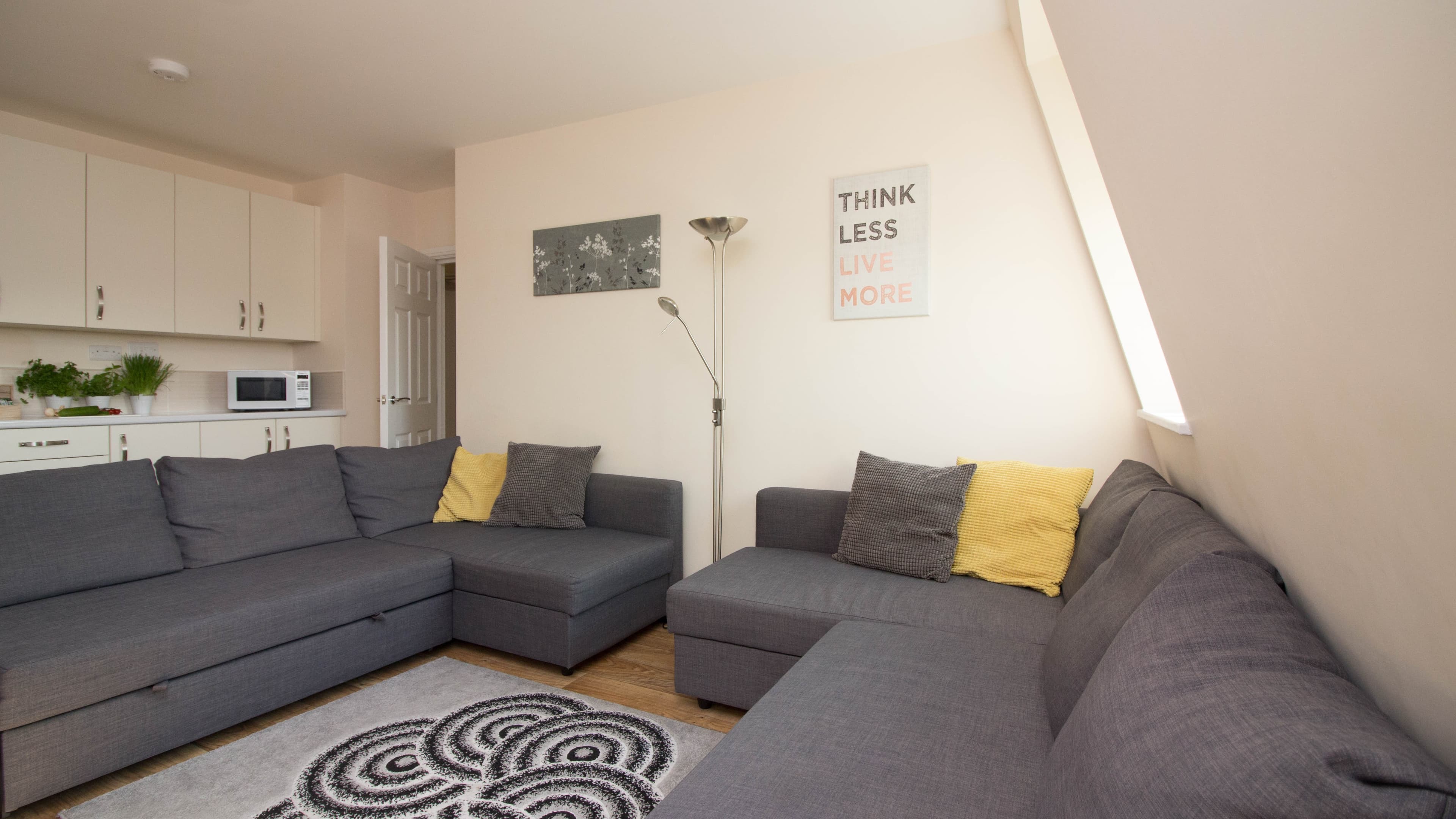 Corner angle of living room with large L-shaped grey sofa, rug, artwork, and window – Castle 17 - Southampton Corner angle of living room with large L-shaped grey sofa, rug, artwork, and window – Castle 17 - Southampton