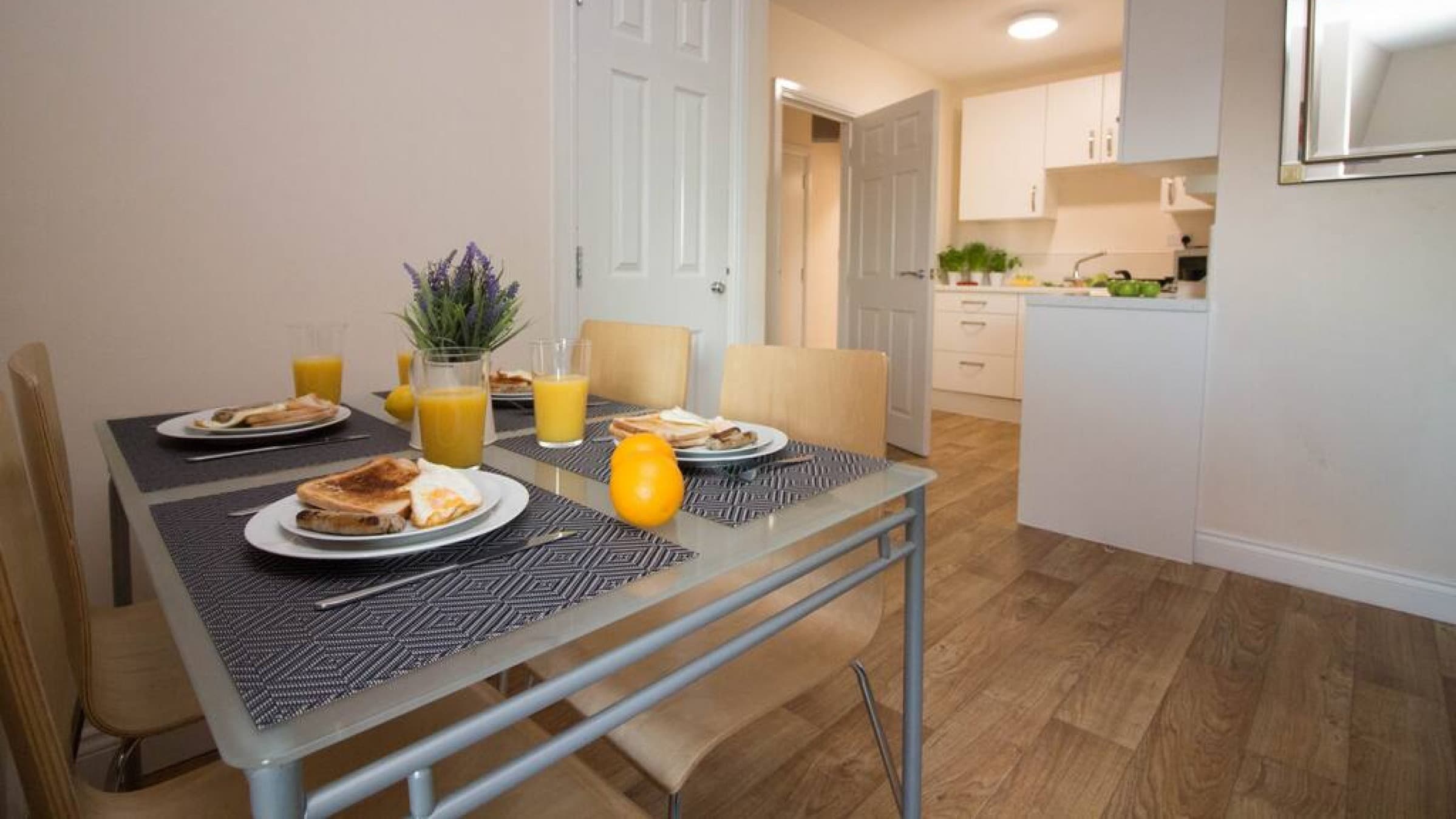 Dining area with place settings for two, fruit, juice, and view to open-plan hallway in modern apartment – Castle 18 - Southampton Dining area with place settings for two, fruit, juice, and view to open-plan hallway in modern apartment – Castle 18 - Southampton
