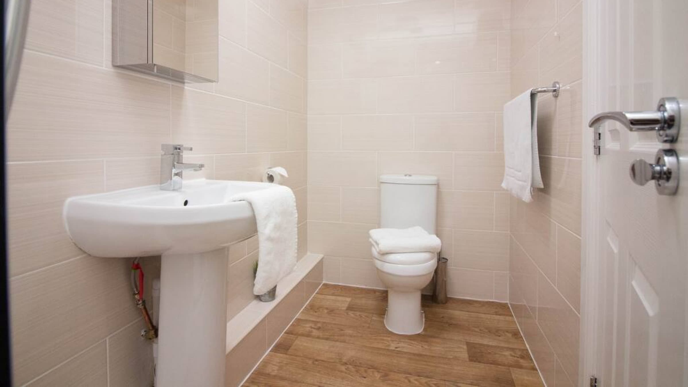 Bathroom with pedestal sink, white toilet, wall-mounted towel rail, and modern tiles – Castle 18 - Southampton Bathroom with pedestal sink, white toilet, wall-mounted towel rail, and modern tiles – Castle 18 - Southampton