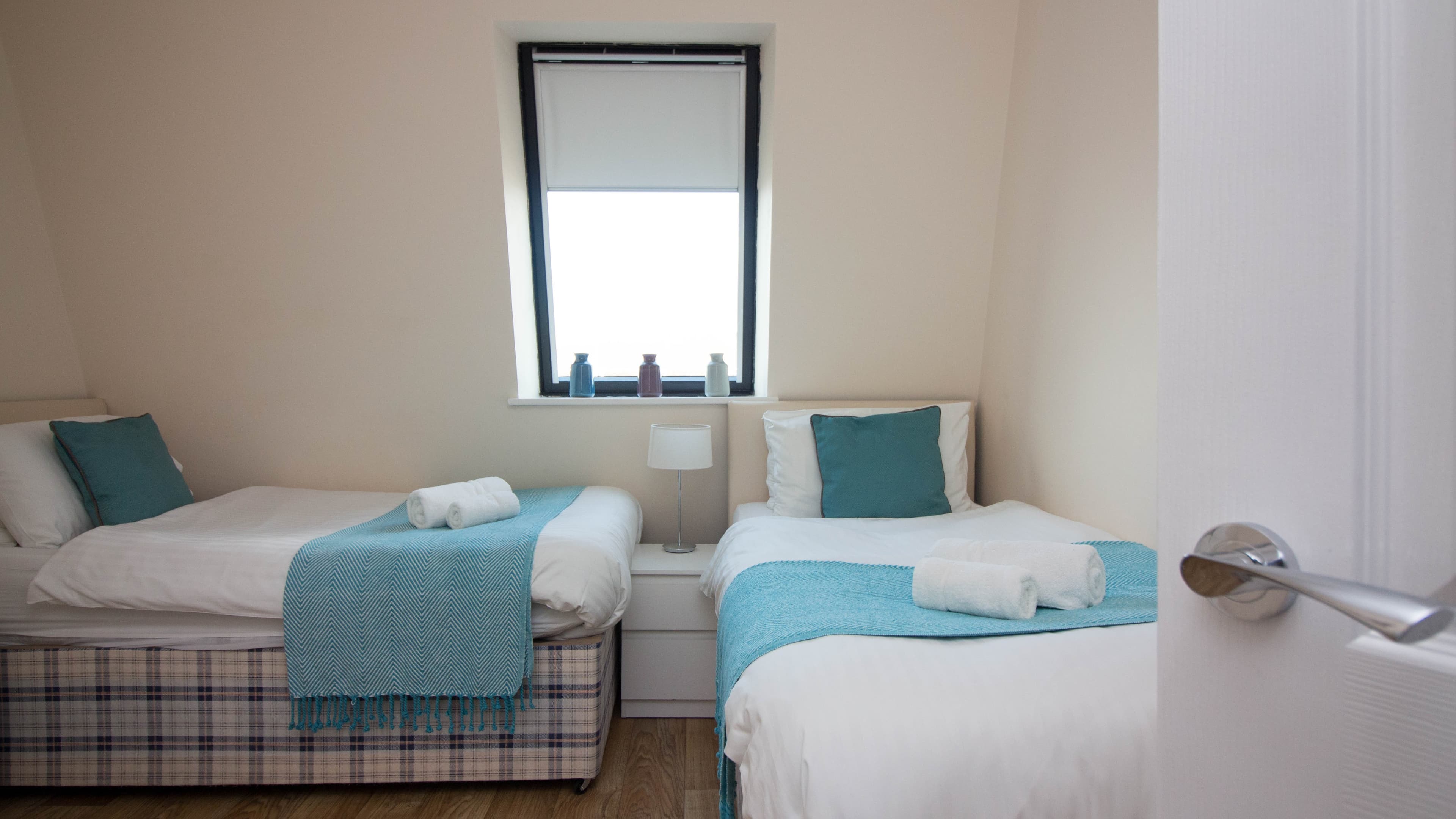 Twin bedroom with matching beds, teal throws, and large window letting in natural light – Castle 19 - Southampton Twin bedroom with matching beds, teal throws, and large window letting in natural light – Castle 19 - Southampton