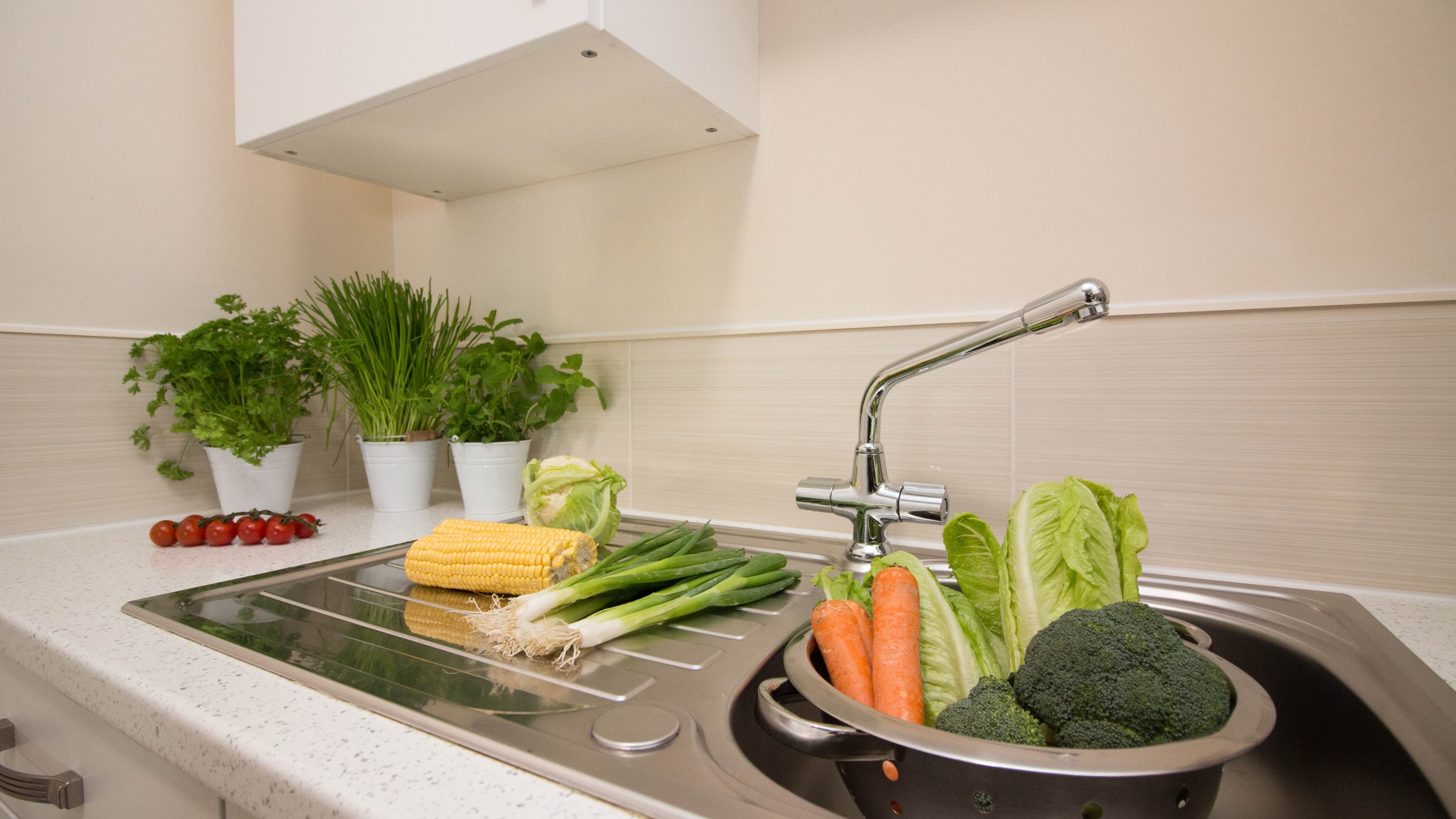 Kitchen sink area with fresh herbs and vegetables on white countertop, serviced apartment kitchen – Castle 19 - Southampton Kitchen sink area with fresh herbs and vegetables on white countertop, serviced apartment kitchen – Castle 19 - Southampton