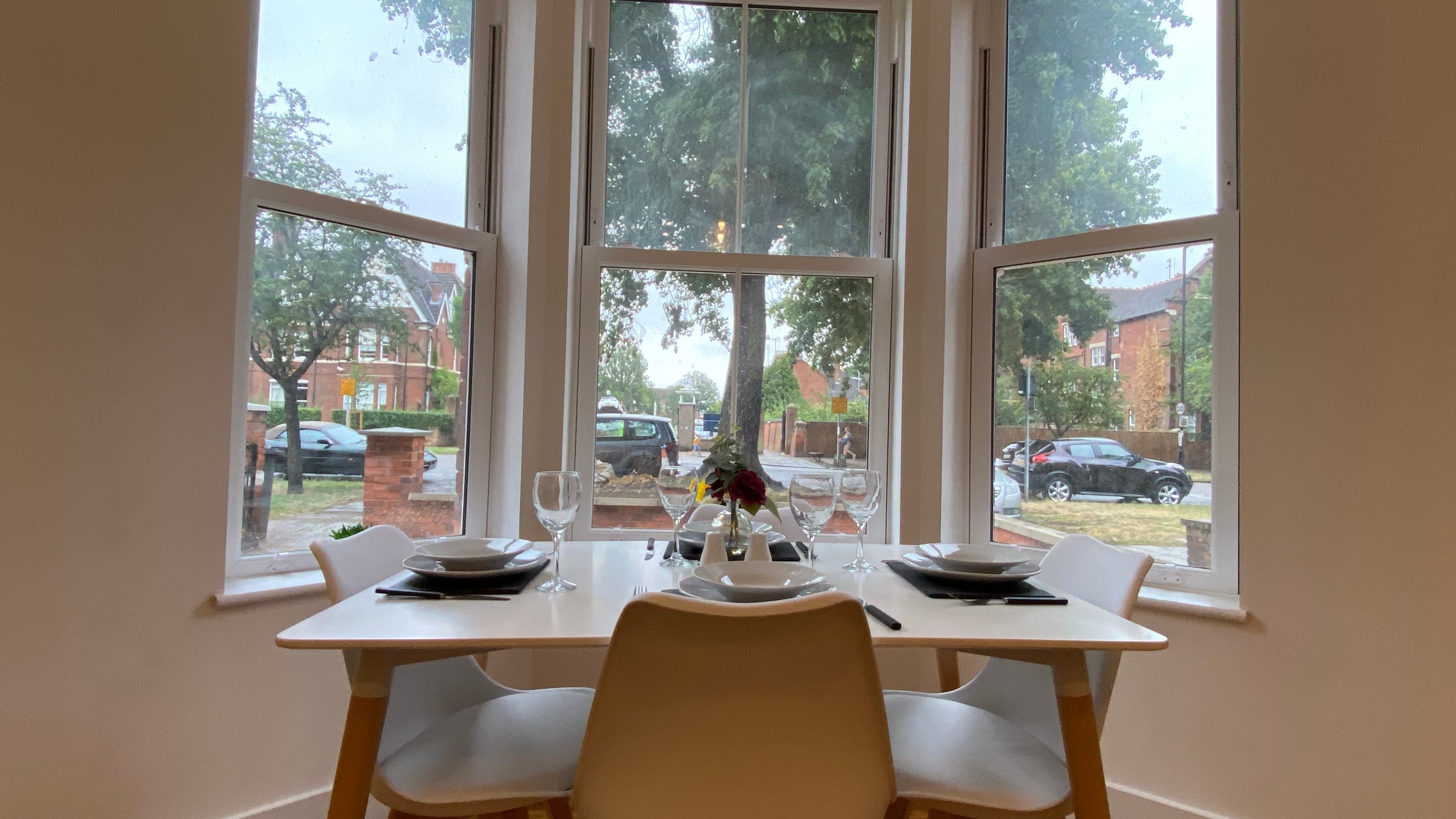 Dining table set for two with white dishes, cutlery, and view through bay windows – De Parys Flat 1, Bedford Dining table set for two with white dishes, cutlery, and view through bay windows – De Parys Flat 1, Bedford