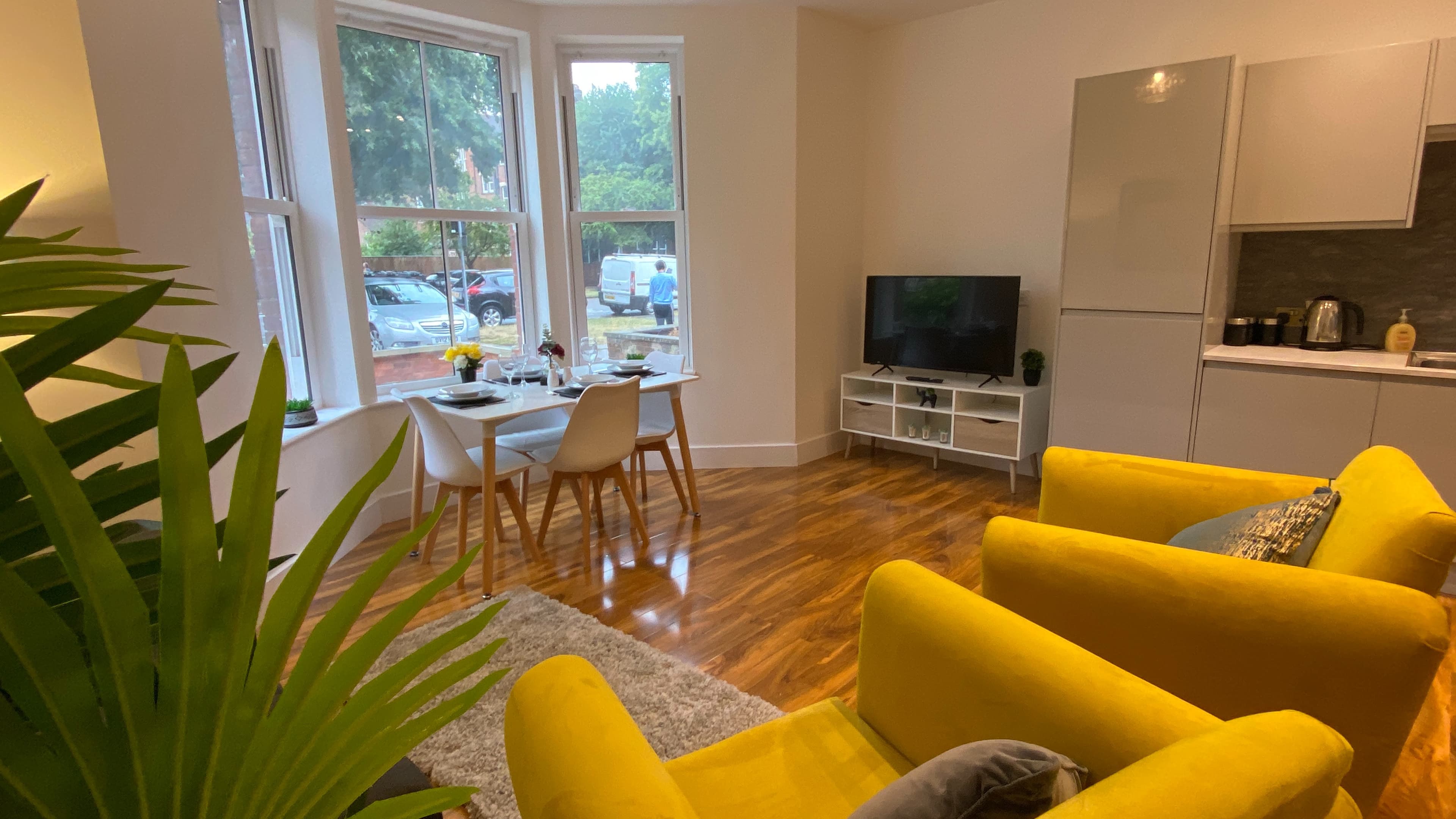 Living space with yellow armchairs, TV, bay window, double bed, and leafy plant – De Parys Flat 1, Bedford Living space with yellow armchairs, TV, bay window, double bed, and leafy plant – De Parys Flat 1, Bedford