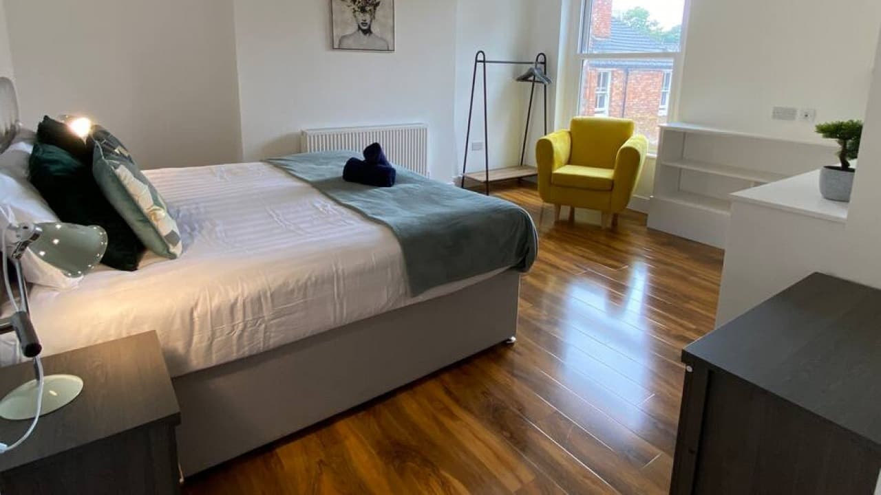 Double bedroom with grey and teal cushions, modern headboard, large window and wooden floor – De Parys Flat 3, Bedford Double bedroom with grey and teal cushions, modern headboard, large window and wooden floor – De Parys Flat 3, Bedford