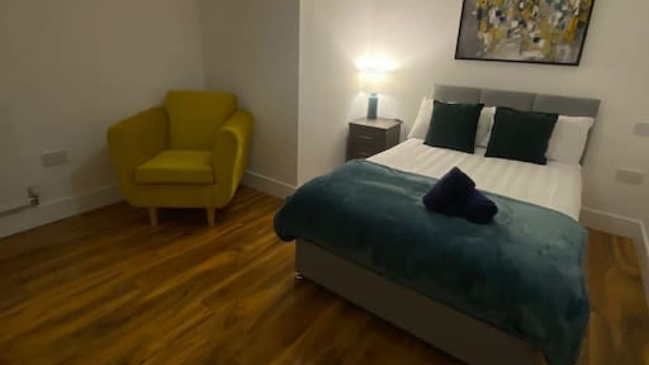 Double bedroom with teal accent pillows, yellow chair, wall art, and wood-effect flooring – De Parys Flat 4, Bedford Double bedroom with teal accent pillows, yellow chair, wall art, and wood-effect flooring – De Parys Flat 4, Bedford