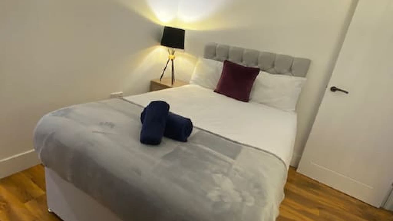 Double bedroom with grey throw, white linens, maroon accent pillow, and modern lamp – De Parys Flat 5, Bedford Double bedroom with grey throw, white linens, maroon accent pillow, and modern lamp – De Parys Flat 5, Bedford