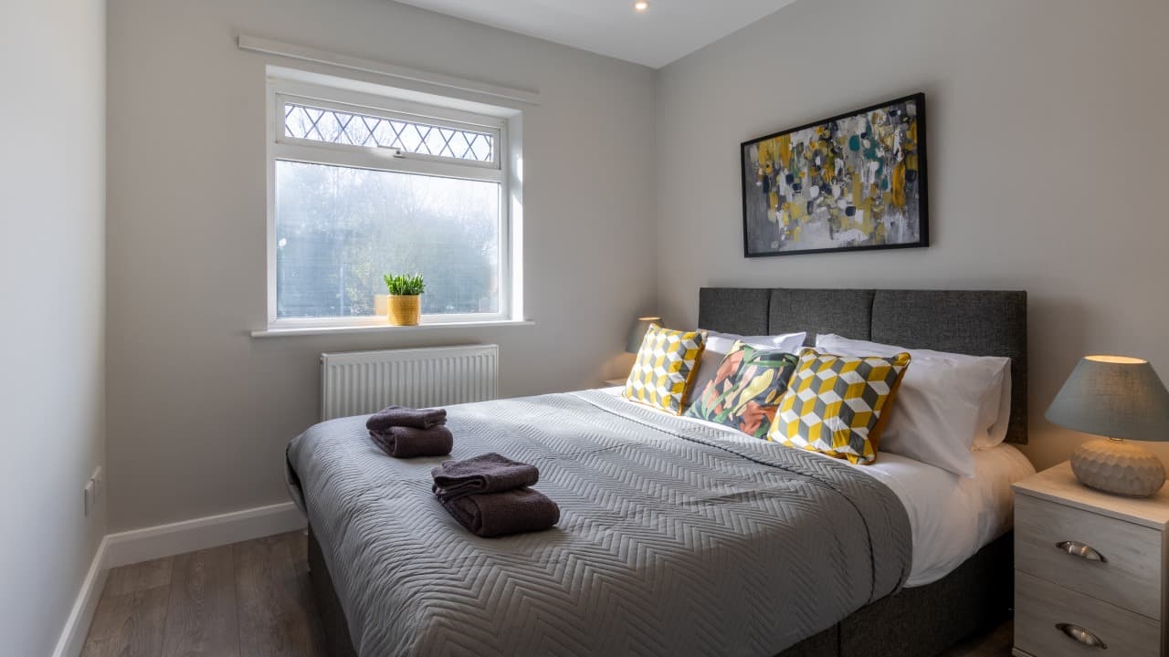 Bright master bedroom with double bed, geometric pillows, and window view at Altham Place bungalow, Morecambe Bright master bedroom with double bed, geometric pillows, and window view at Altham Place bungalow, Morecambe