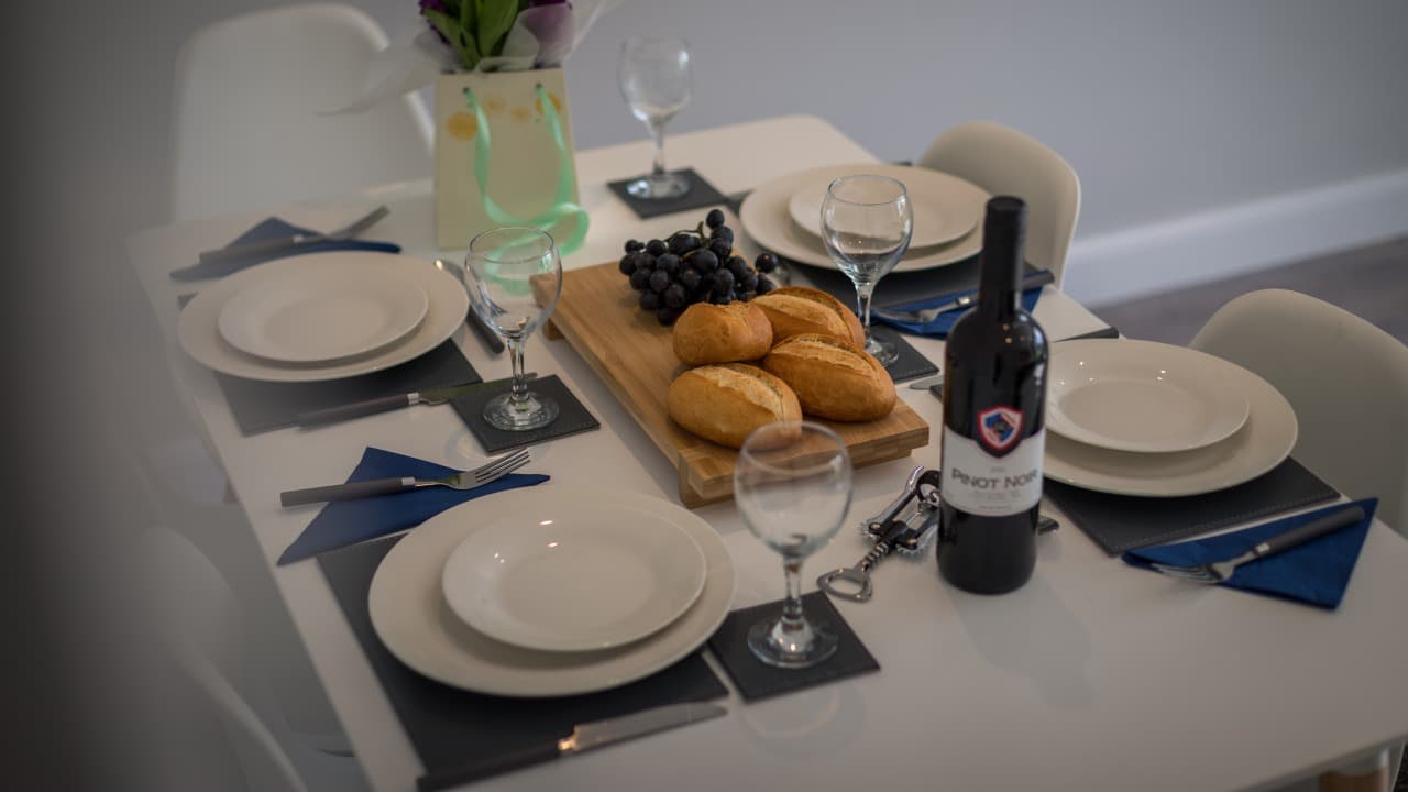Elegant dining table set with wine, bread rolls, grapes, and white crockery in Altham Place bungalow, Morecambe Elegant dining table set with wine, bread rolls, grapes, and white crockery in Altham Place bungalow, Morecambe